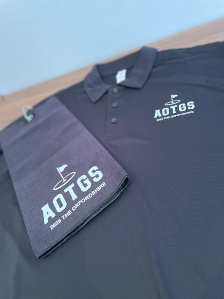 Dark blue polo shirt and towel with AOTGS branding on a Black background